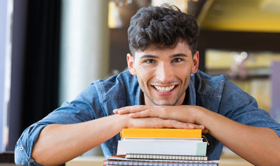 Junger Mann stützt sich auf einen Stapel Bücher
