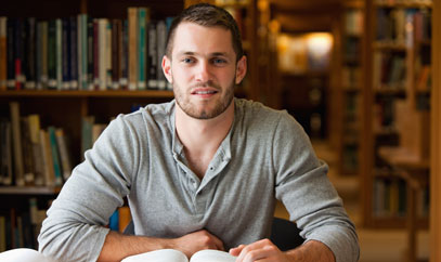 Junger Mann mit aufgeschlagenem Buch in einer Bibliothek.